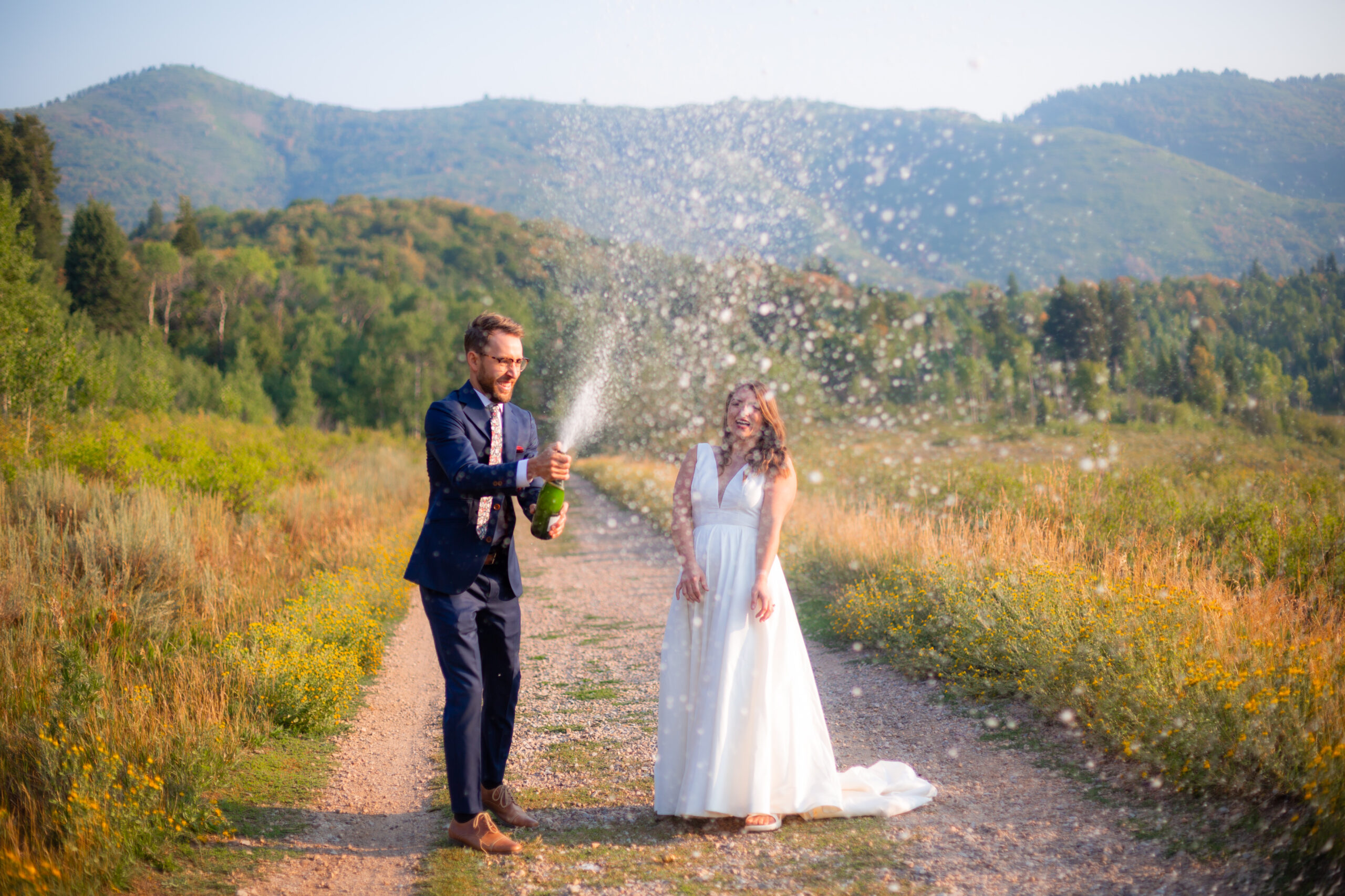 Chiha Studios wedding photography of a couple on their wedding day outside in the mountains opening a bottle of champagne