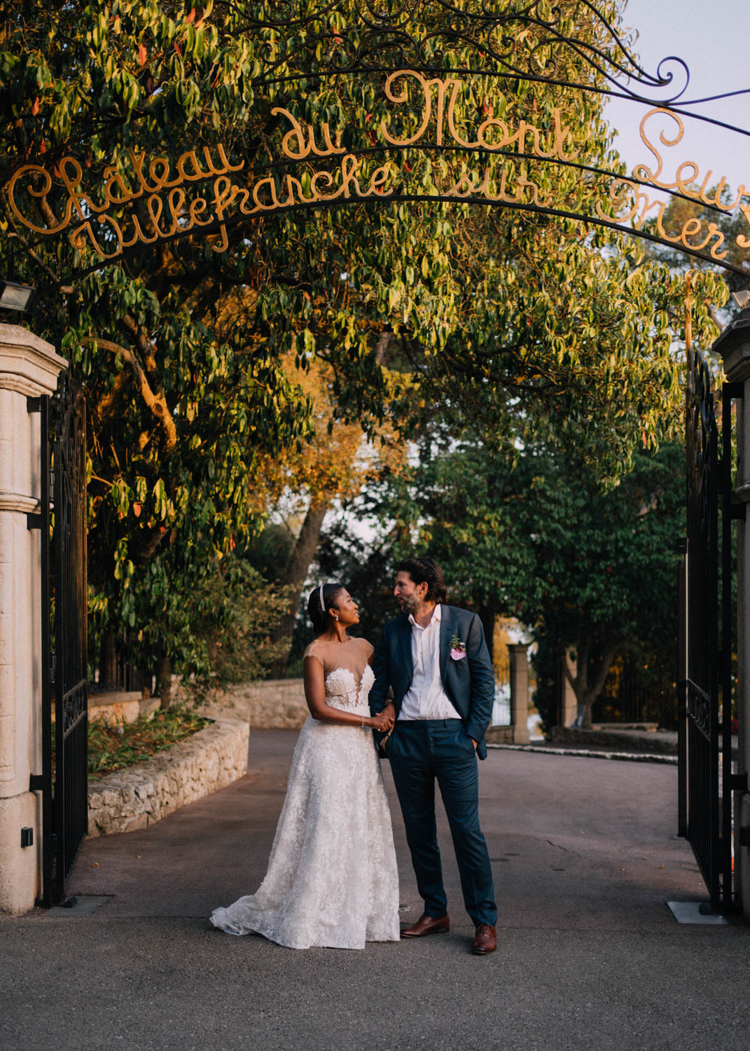 A bride and groom walk under the Domaine du Mont Leuze entrance arch