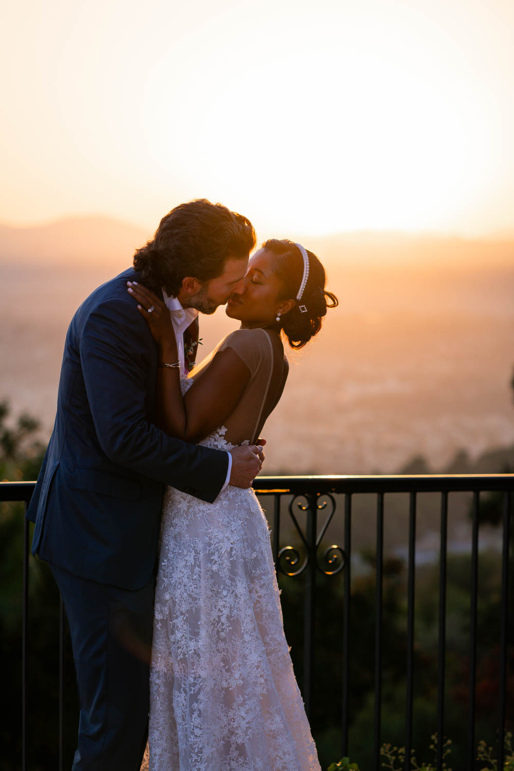Newlyweds kiss at sunset on a balcony overlooking the city