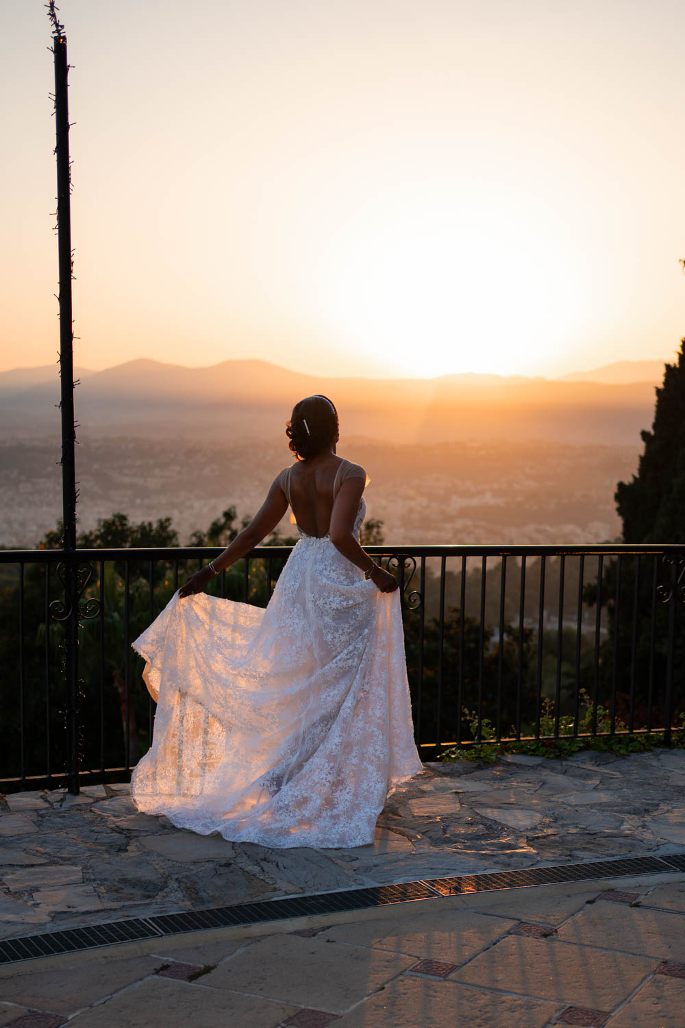 A happy bride watches the sunset behind the mountains in her long lace gown