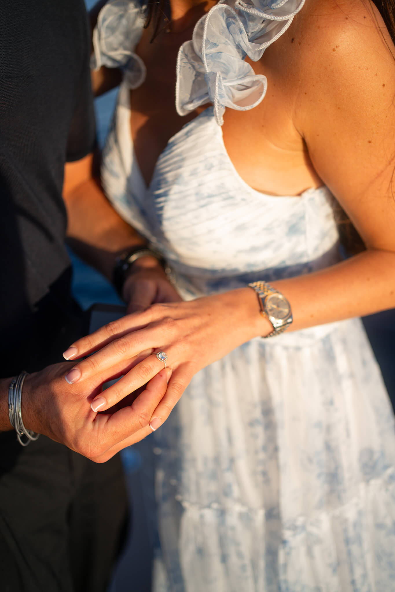 Details of a woman's hand with engagement ring while wearing a blue and white dress