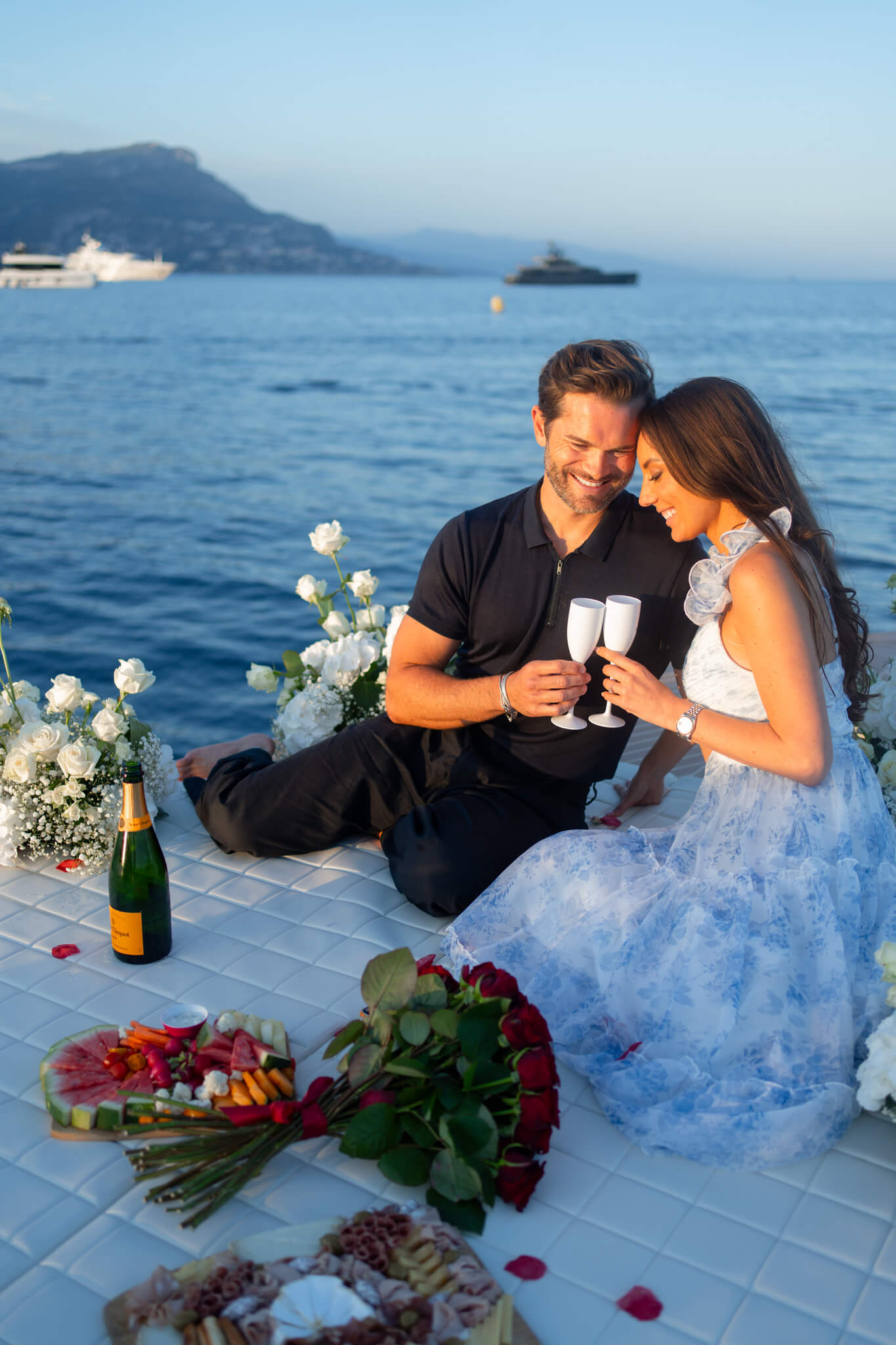 A happy couple sits on a boat toasting champagne with big smiles at sunset