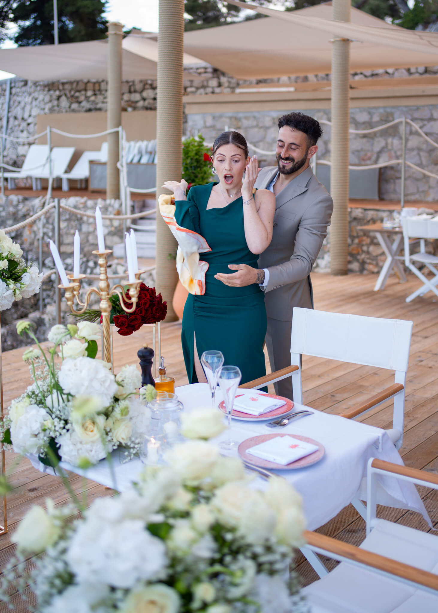 A man and woman arrive at a private balcony dinner set up with white bouquets
