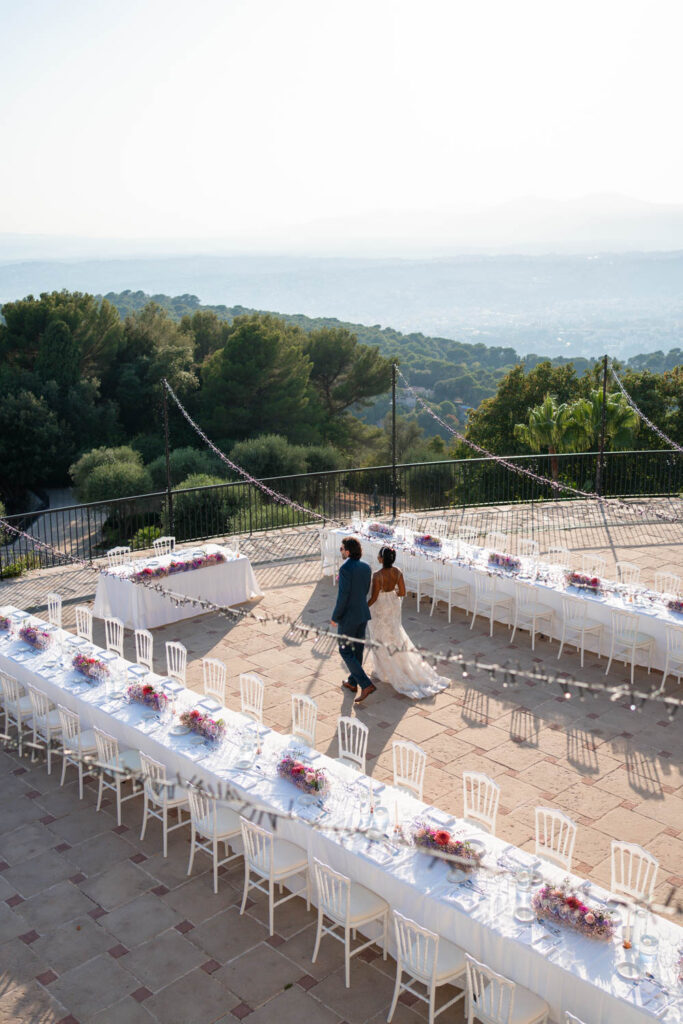 Newlyweds walk through their outdoor reception space set up under market lights on a balcony at one of the Wedding Venues In Nice France